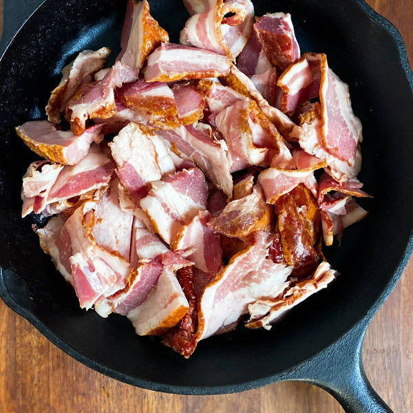 Raw bacon pieces in a black cast iron skillet on a wooden surface