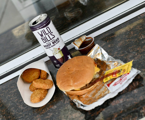 Burger, fries, and root beer on a table near a window