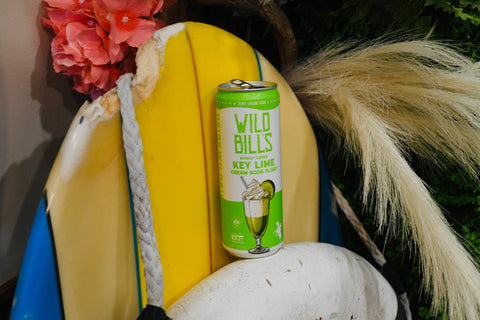 Can of Wild Bill's Key Limeade on a surfboard with flowers and pampas grass in the background