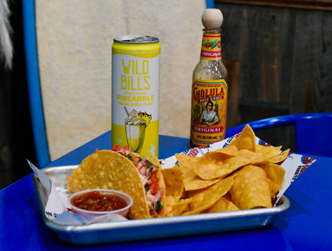 Tray with tacos, chips, salsa, and a can of Wild Bills Pineapple Juice on a blue tray.