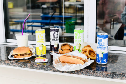 Food and drinks on a counter with Wild Bills root beer cans in the foreground.