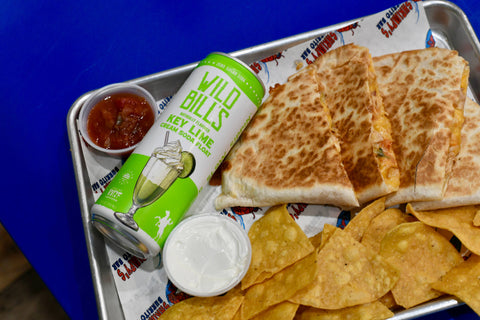 Tray with quesadillas, chips, and a can of Wild Bill's Margaritas on a blue surface.