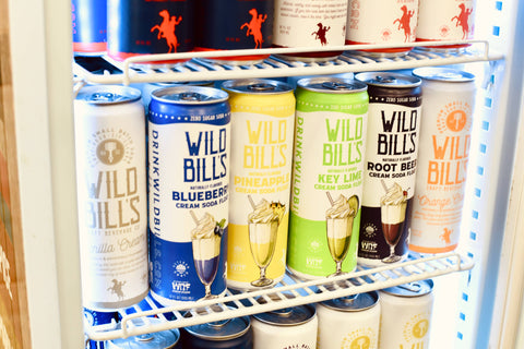 Assorted cans of Wild Bills drinks on a refrigerator shelf.