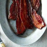 Bacon strips on a white plate with a fork on a textured surface
