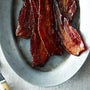 Bacon strips on a white plate with a fork on a textured surface