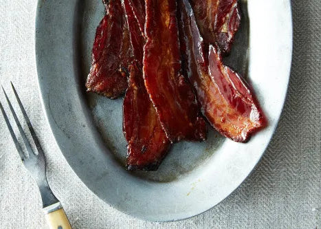 Bacon strips on a white plate with a fork on a textured surface