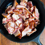 Raw bacon pieces in a black cast iron skillet on a wooden surface