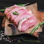 Raw pork chops on a wooden board with herbs and spices on a dark surface