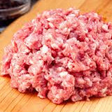 Raw ground meat on a wooden cutting board with spices in the background