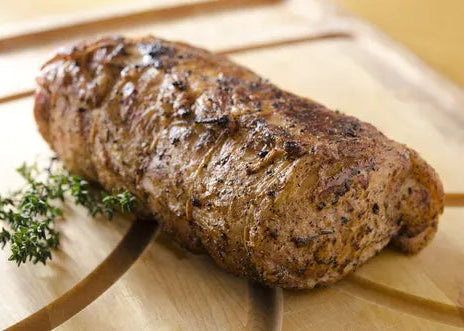 Grilled meatloaf on a wooden cutting board with herbs