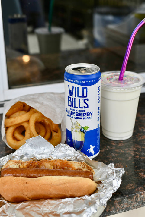 Can of Wild Bill's Blueberry Cream Soda Float with onion rings, hot dog, and drink on a table.