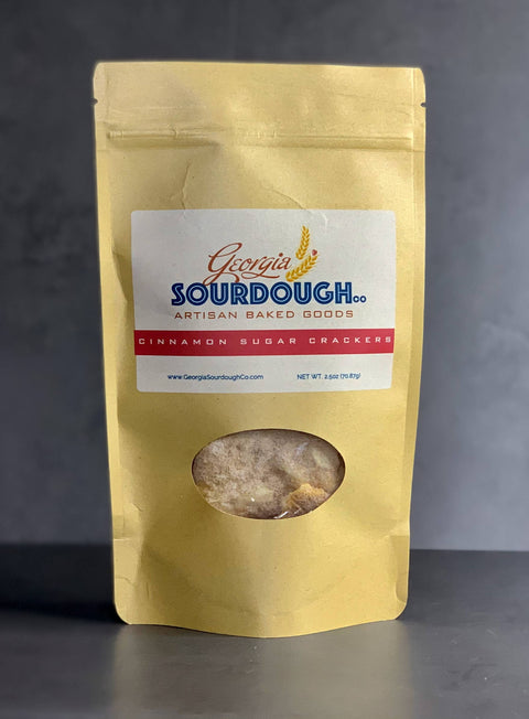 Gold packaging of Georgia Sourdough crackers with a clear window showing the crackers inside on a dark background.